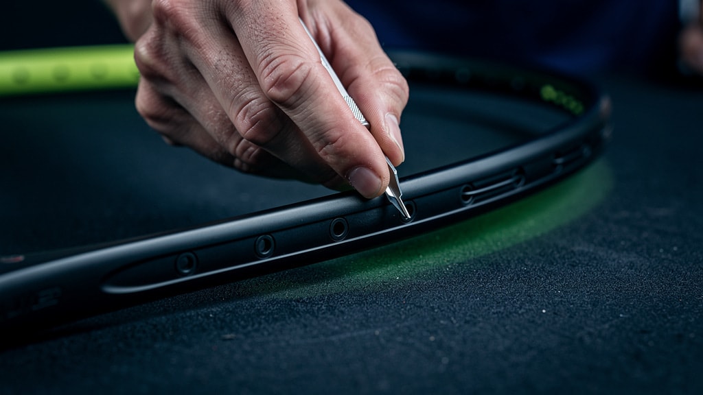 A technician inspecting the grommets on a badminton racket frame